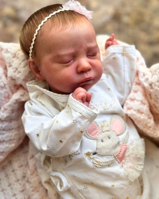 Abbie Annette Silicone Baby Doll dressed in white outfit with mouse embroidery, wearing a headband, lying with arms raised